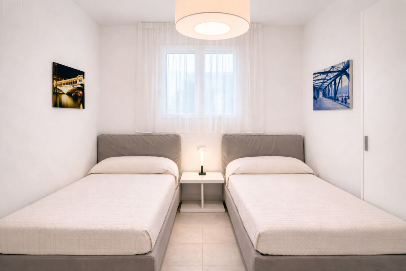 A twin bedroom with two beds, a nightstand, a lamp, and two framed pictures on the walls.