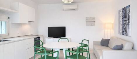 A modern kitchen with white cabinets, a dining table with green chairs, a flat-screen TV, and a white sofa.