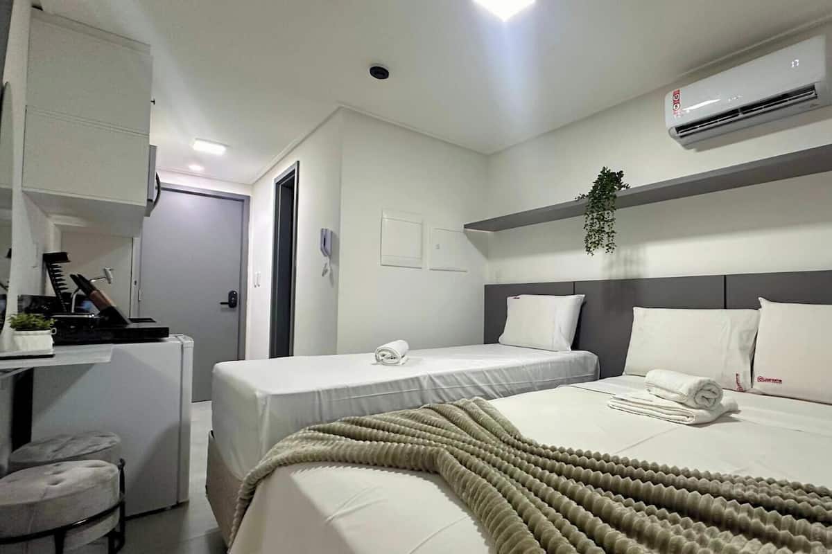 Una habitación de hotel con cama, escritorio, silla, mesita pequeña, equipo de aire acondicionado y una planta.