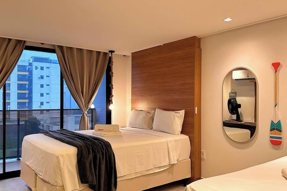 Habitación de hotel con una cama, una cama individual, un ventanal grande, un espejo y un perchero en la pared.