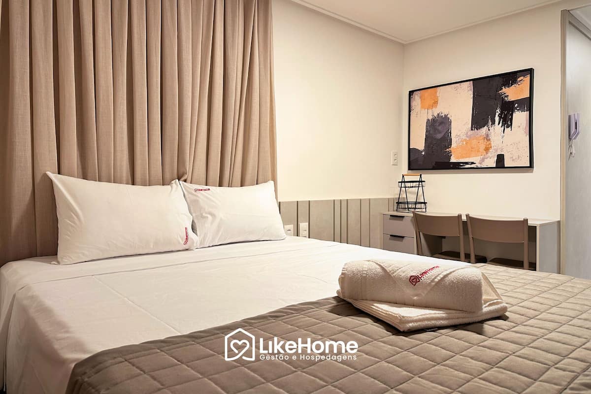 Habitación de hotel con cama, dos almohadas, colchón acolchado, escritorio con silla y un cuadro en la pared.