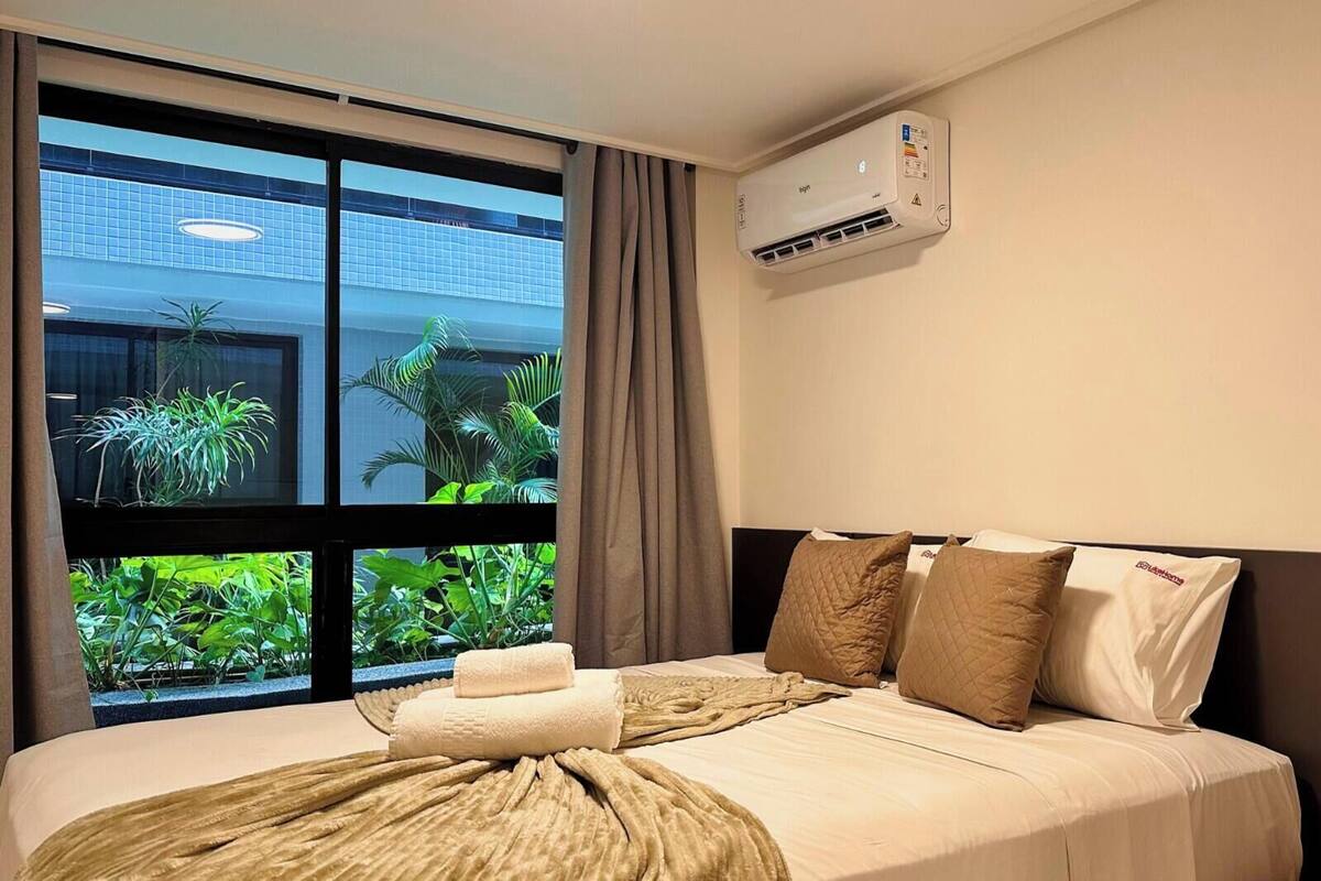 Una habitación de hotel con una cama, un ventanal con vistas a zonas verdes y un equipo de aire acondicionado.
