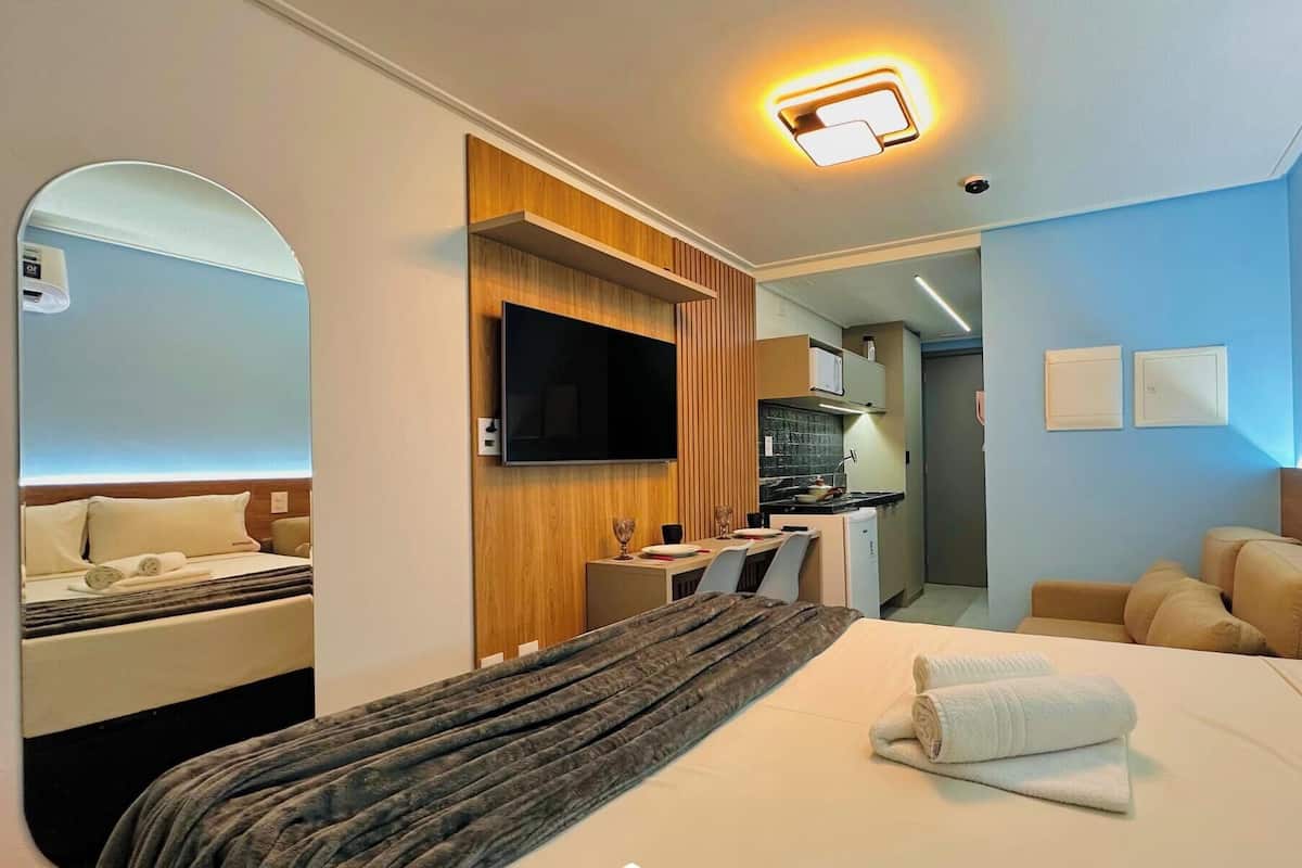 Una habitación de hotel con cama, televisor, escritorio y kitchenette.