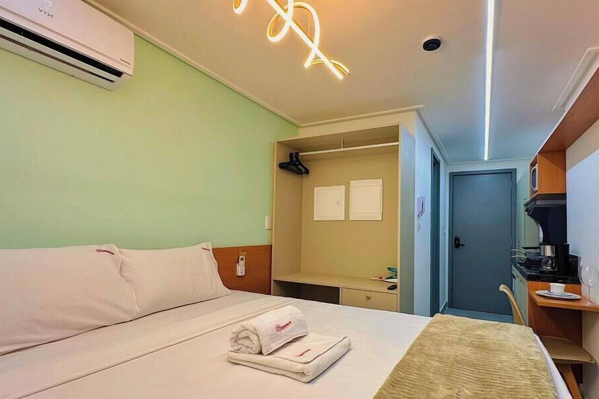 Habitación de hotel con cama, mesita de noche, escritorio con silla, espejo y aire acondicionado.