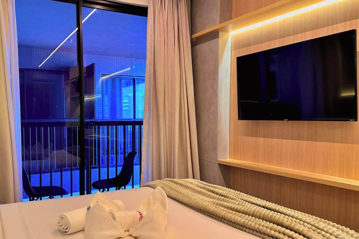 Una habitación de hotel con cama, televisión, ventana con cortinas y vistas al exterior.