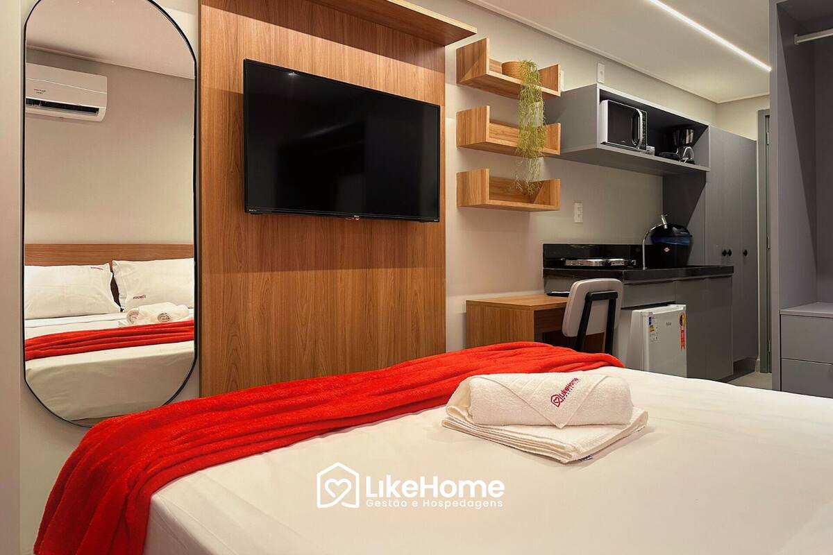 Una habitación de hotel con cama, televisión, kitchenette pequeña y espejo.