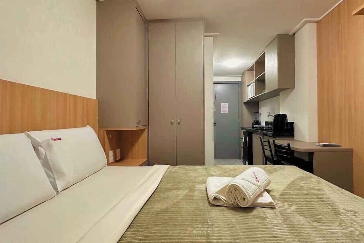 Una habitación de hotel con una cama, un escritorio pequeño, una kitchenette y una puerta que da a un baño.