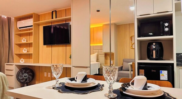 A hotel room with a dining area, a TV, a coffee machine, and a minibar. - Hit Cabo Branco III - LikeHome (João Pessoa)