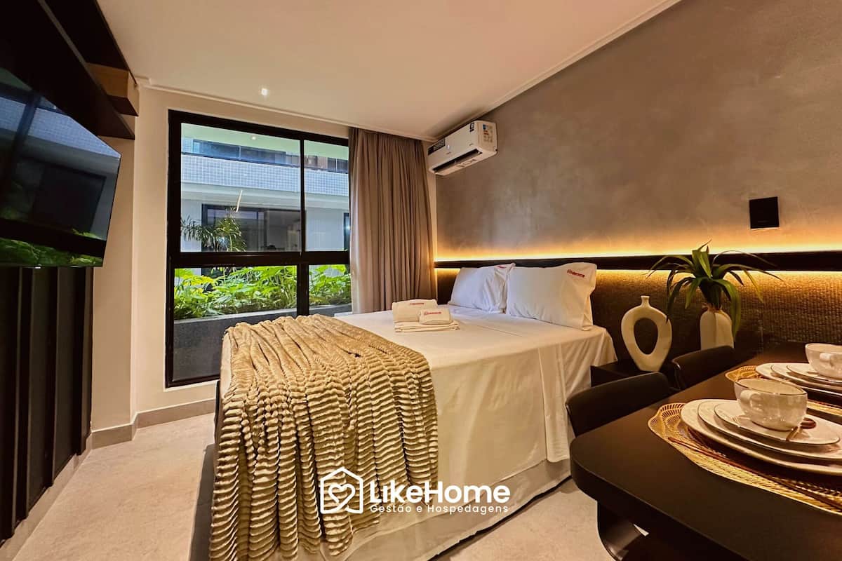 Una habitación de hotel moderna con una cama grande, un televisor de pantalla plana, un comedor con mesa puesta y vistas a zonas verdes.