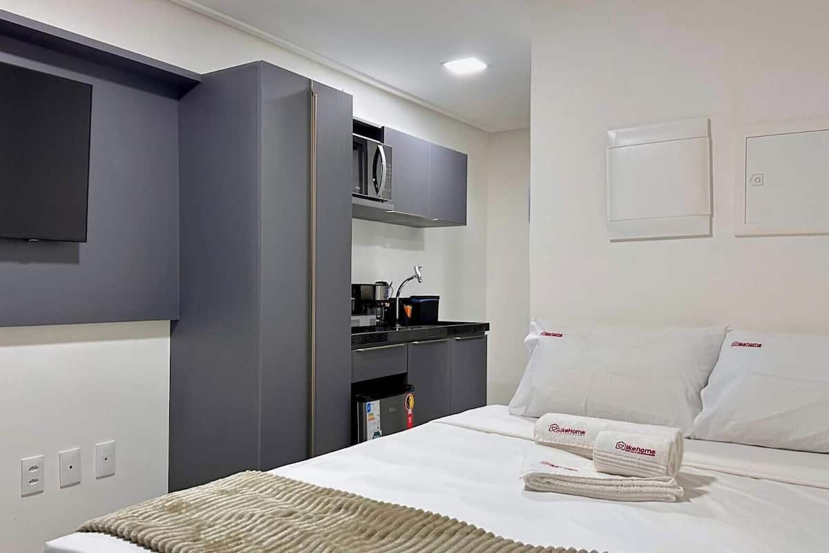 Una habitación de hotel moderna con cama, televisión de pantalla plana, microondas integrado y una pequeña cocina.