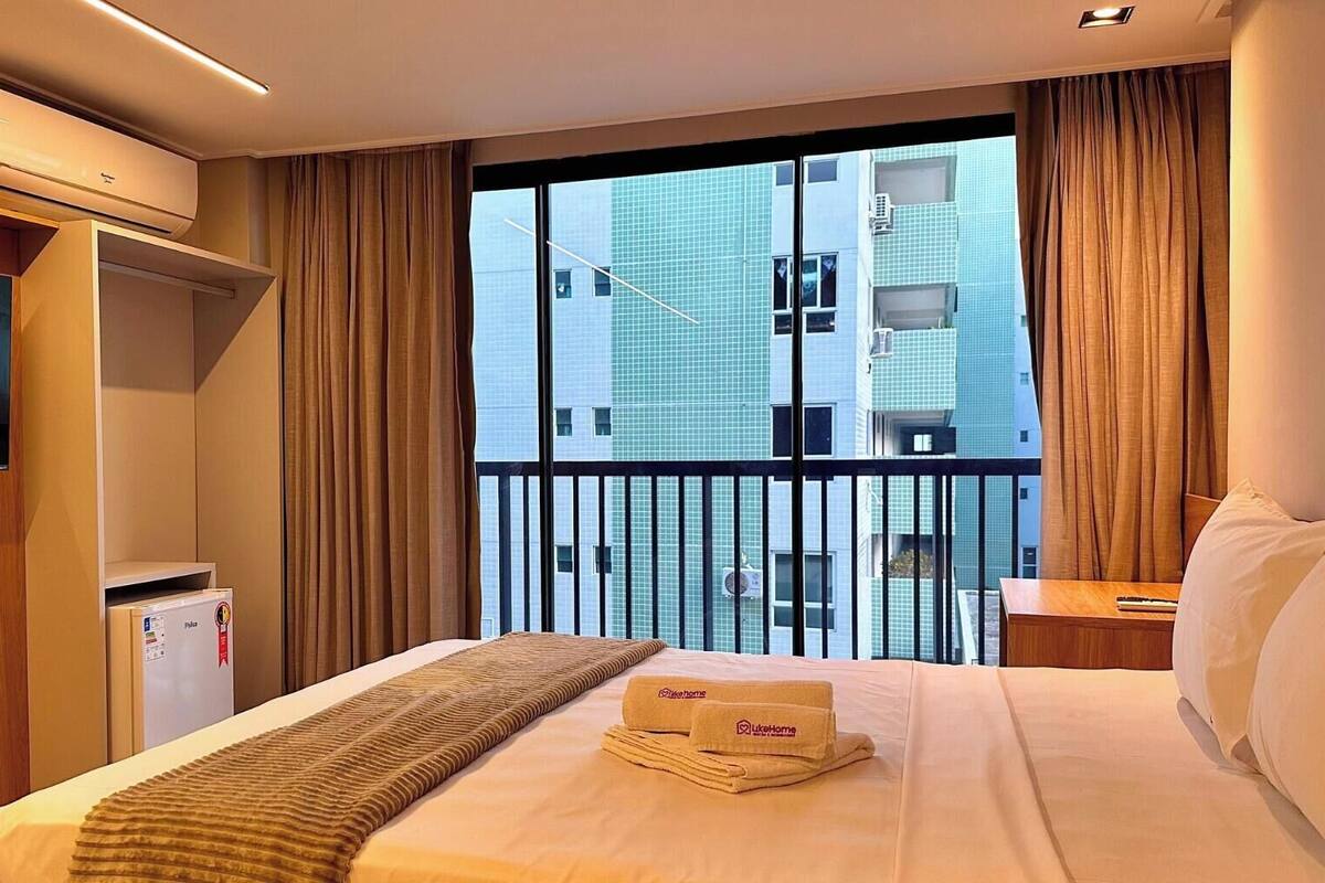 Habitación de hotel con cama, televisión, aire acondicionado, minibar y ventana con vista a un edificio.