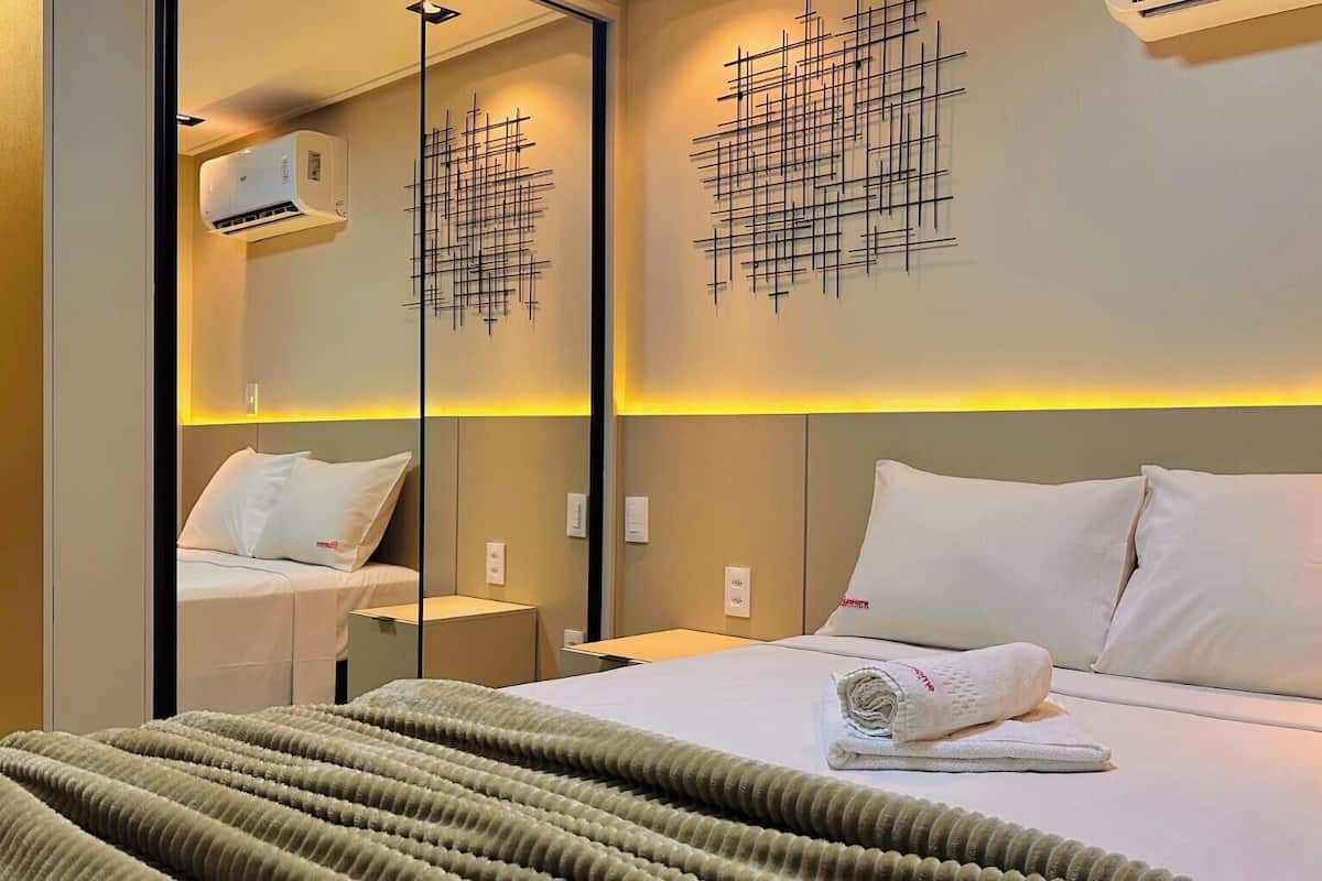 Habitación de hotel con cama, espejo, una obra de arte en la pared y aire acondicionado instalado en la pared.