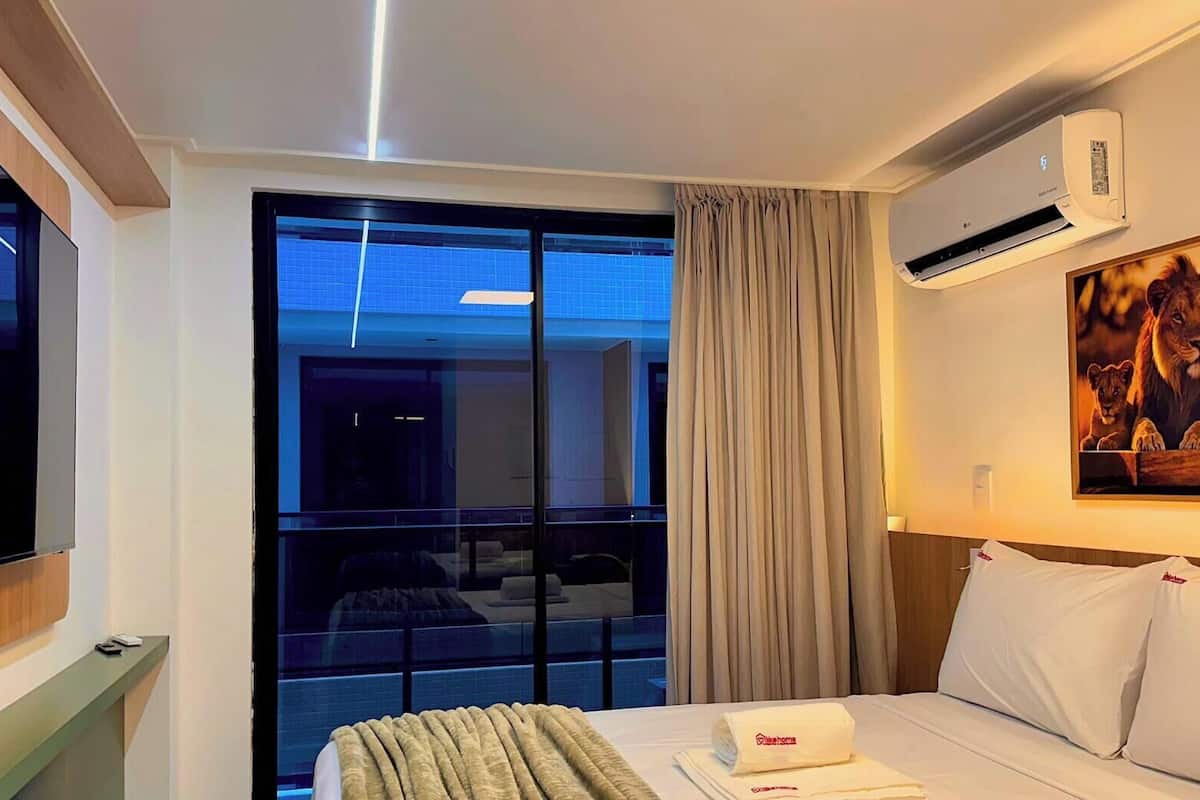 Habitación de hotel con cama, televisión, aire acondicionado, un cuadro y vista a la piscina.