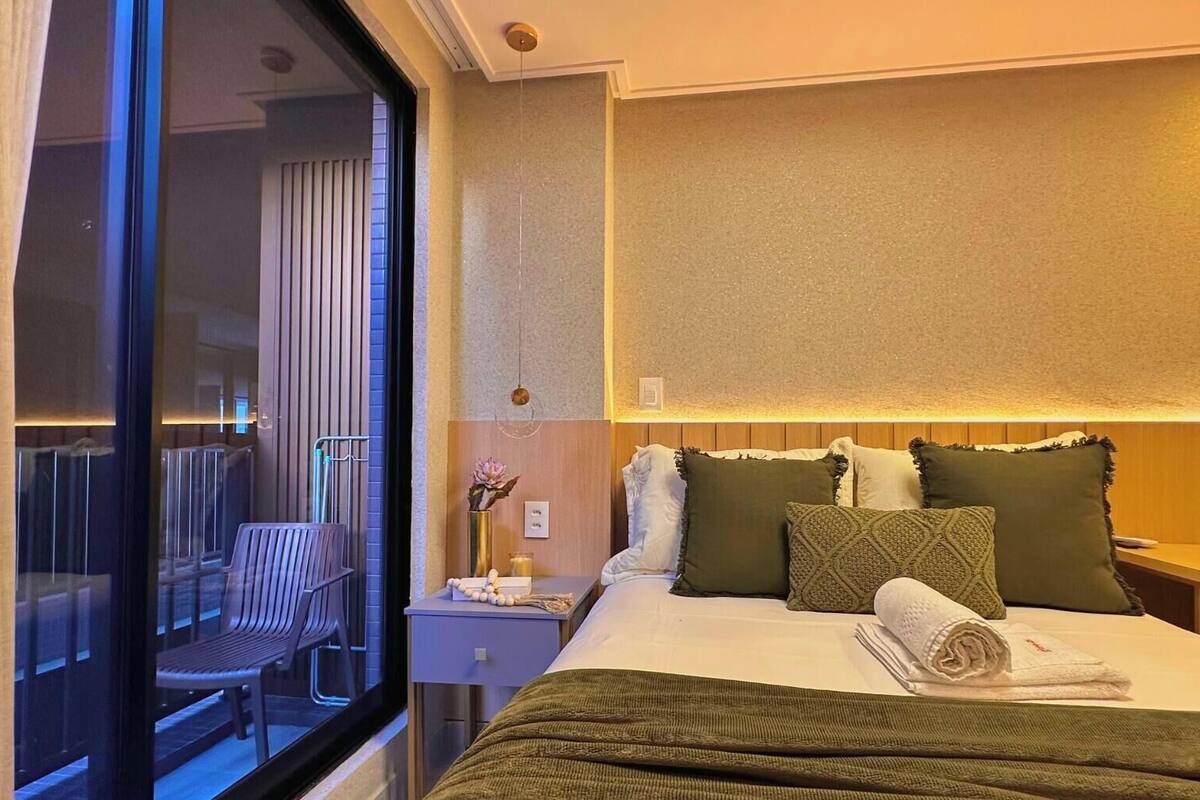 Habitación de hotel con cama, escritorio, silla, mesita de noche y ventana con vistas al exterior.
