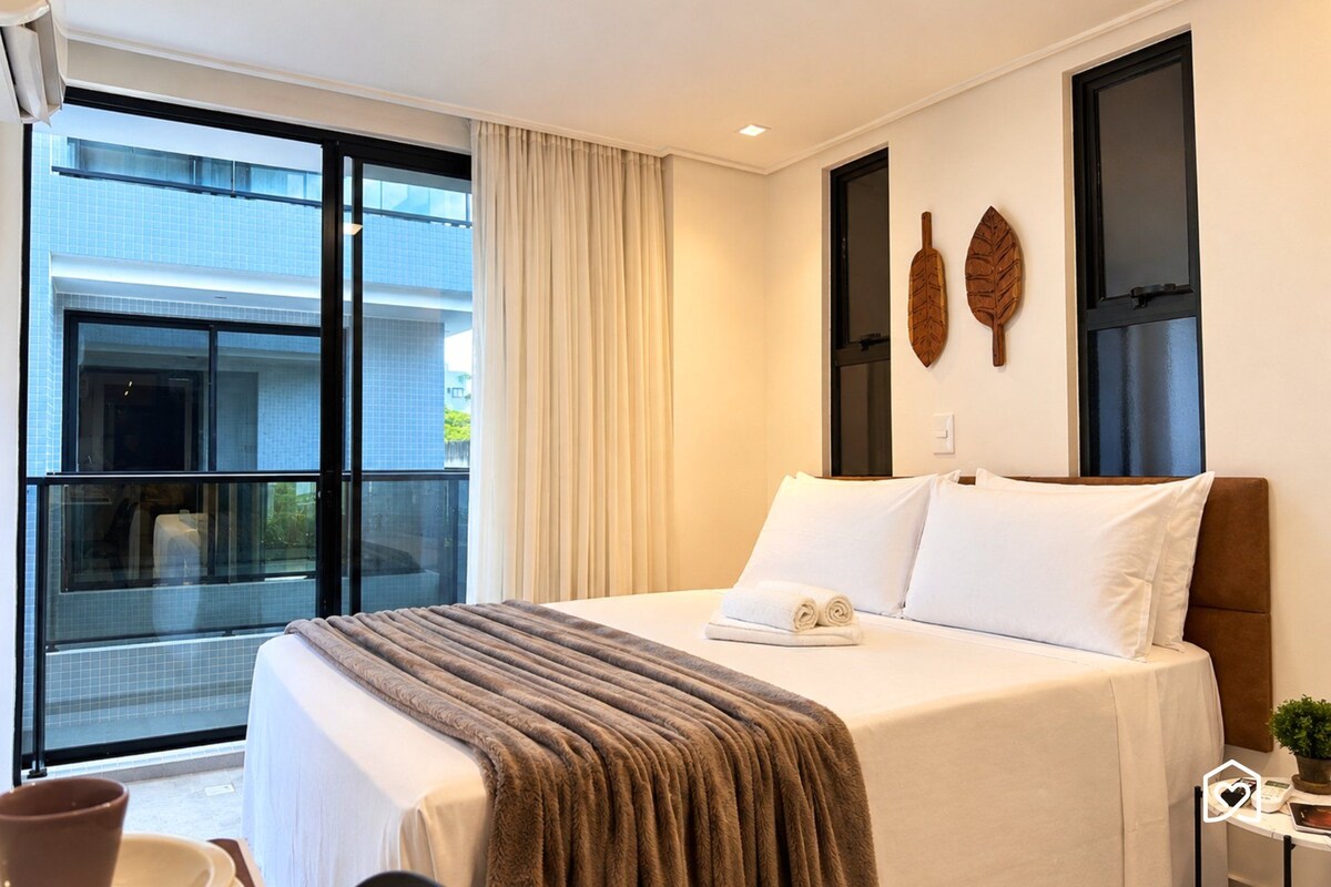 A hotel room with a large bed, a window with a view of buildings, and a small table with a plant.
