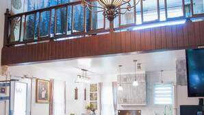 Un ampio soggiorno con soffitto alto, un lampadario, un tavolo da pranzo con sedie, una zona cucina e un televisore.