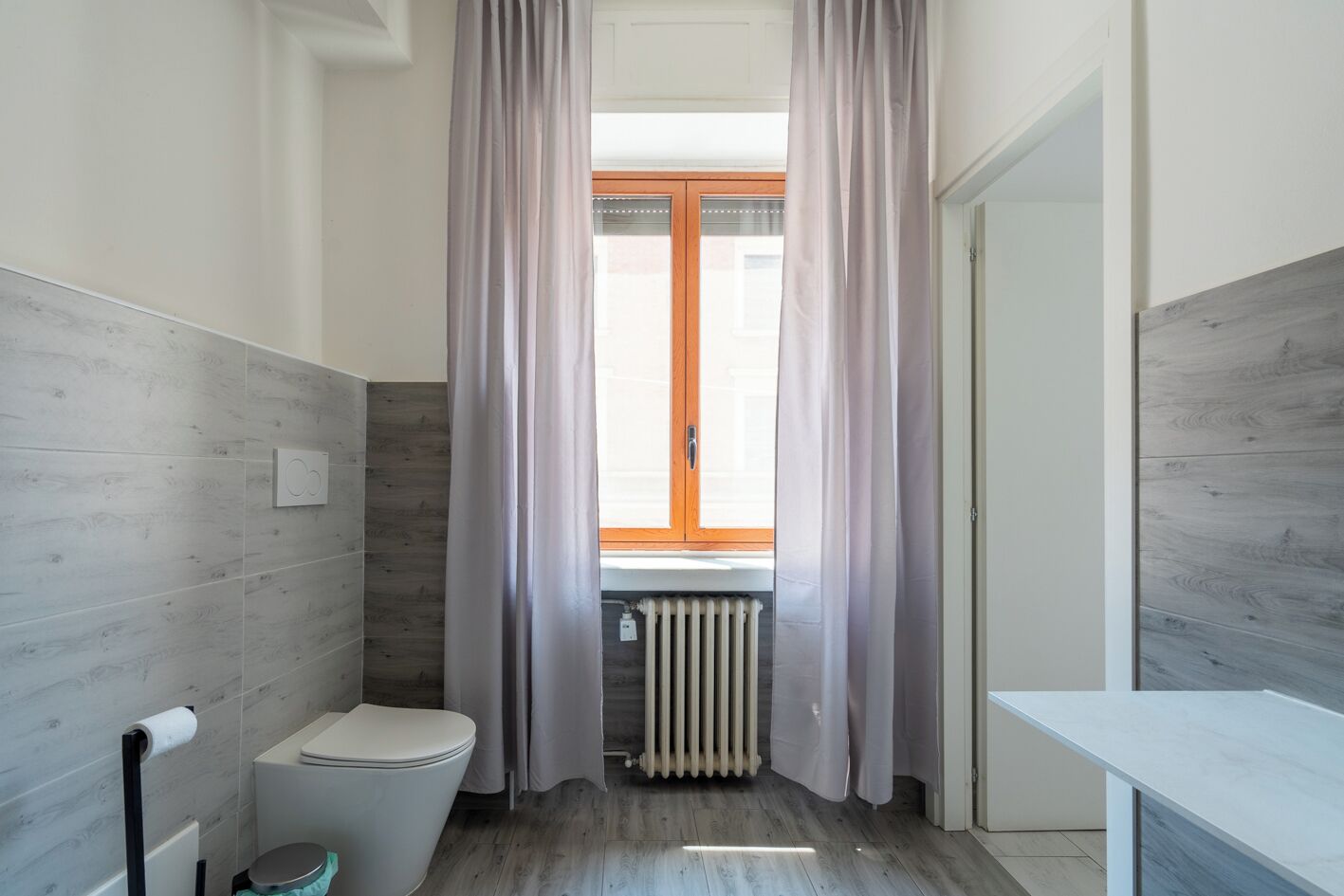 Ein Badezimmer mit Toilette, Heizkörper und einem Fenster mit Vorhängen.
