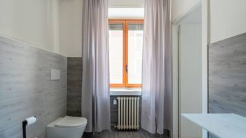 Ein Badezimmer mit Toilette, Heizkörper und einem Fenster mit Vorhängen.