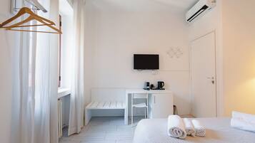 A hotel room with a bed, a desk, a chair, a TV, and a coffee maker.