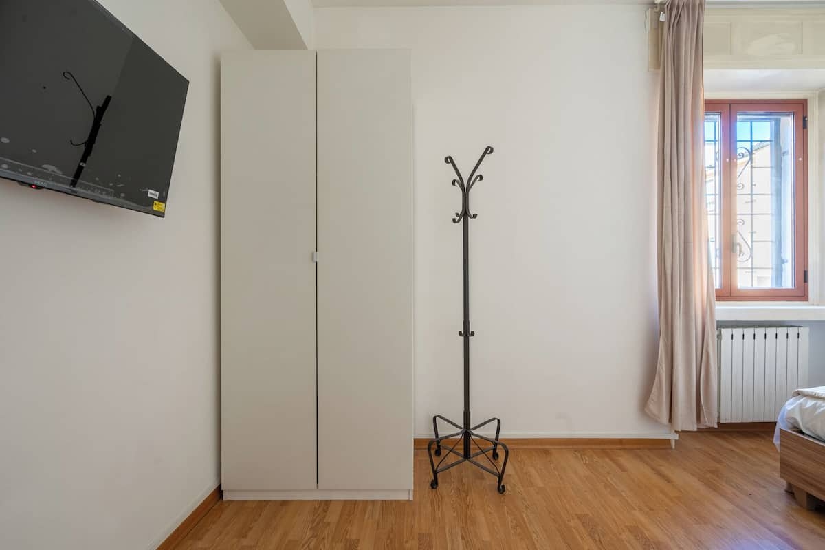 Une pièce comprenant une armoire, un porte-manteau, un lit et une fenêtre avec des rideaux.