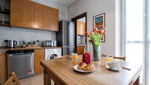 Ett modernt kök med träskåp, vitvaror i rostfritt stål och ett matbord dukat med croissanter, en röd mugg och en vas med tulpaner.