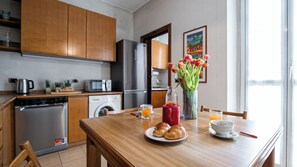 A modern kitchen with wooden cabinets, stainless steel appliances, and a dining table set with croissants, a red mug, and a vase of tulips. - Italianway Easy - Strambio 8 (Milan)