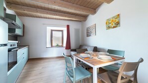 A modern kitchen with wooden beams, a dining area with a table set for two, and a cozy living space with a sofa.