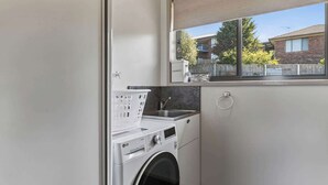 A compact laundry area with a washing machine, a drying rack, and a window with a view of neighboring houses. - The Blue Window - 15 Mins to CBD&Airport (Howrah)