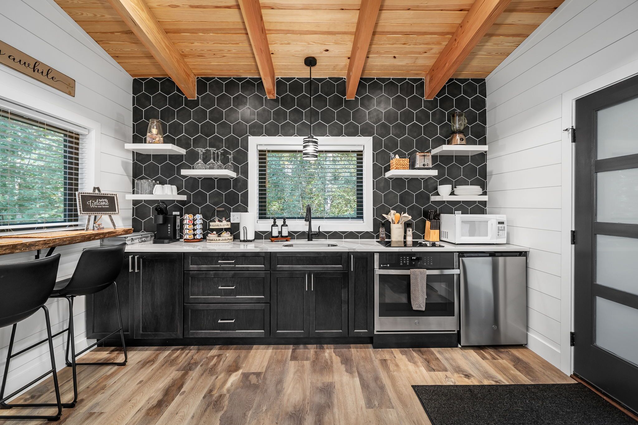 A compact kitchen with dark cabinets, a wooden ceiling, and a window with a view.