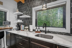 A modern kitchen with a black and white hexagonal tile backsplash, a stainless steel sink, and a window with blinds.