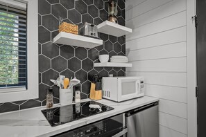A modern kitchen with a black hexagonal tile backsplash, white cabinetry, a built-in microwave, and a black induction cooktop.