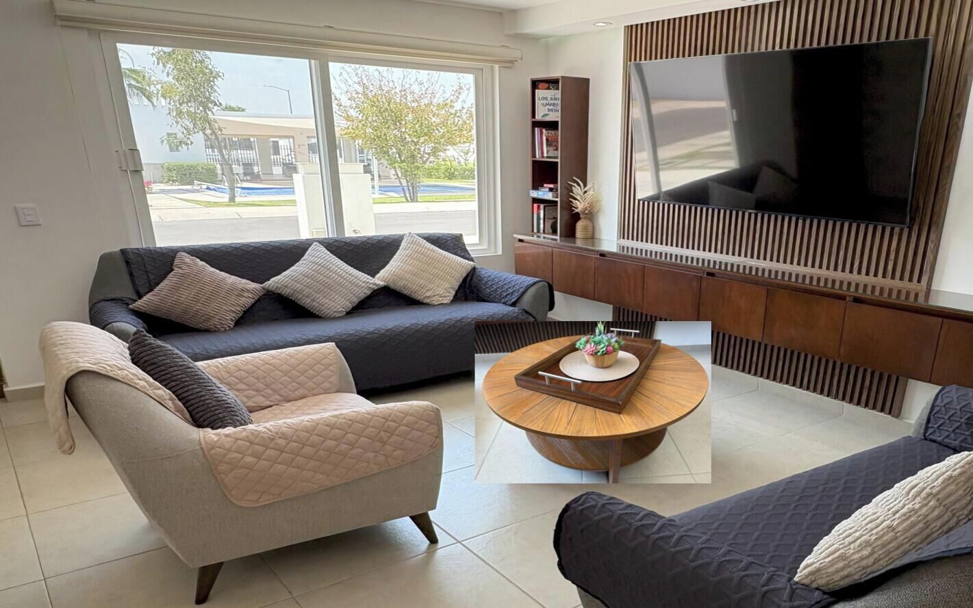 A modern living room with a large flat-screen TV, a round coffee table, and two sofas with cushions.
