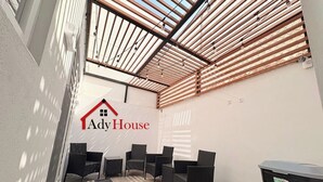 Uma área de estar coberta ao ar livre, com cadeiras de vime e uma lixeira, identificada como "Ady House".