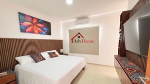 Quarto de hotel com cama, televisão, pintura e um logotipo na parede.