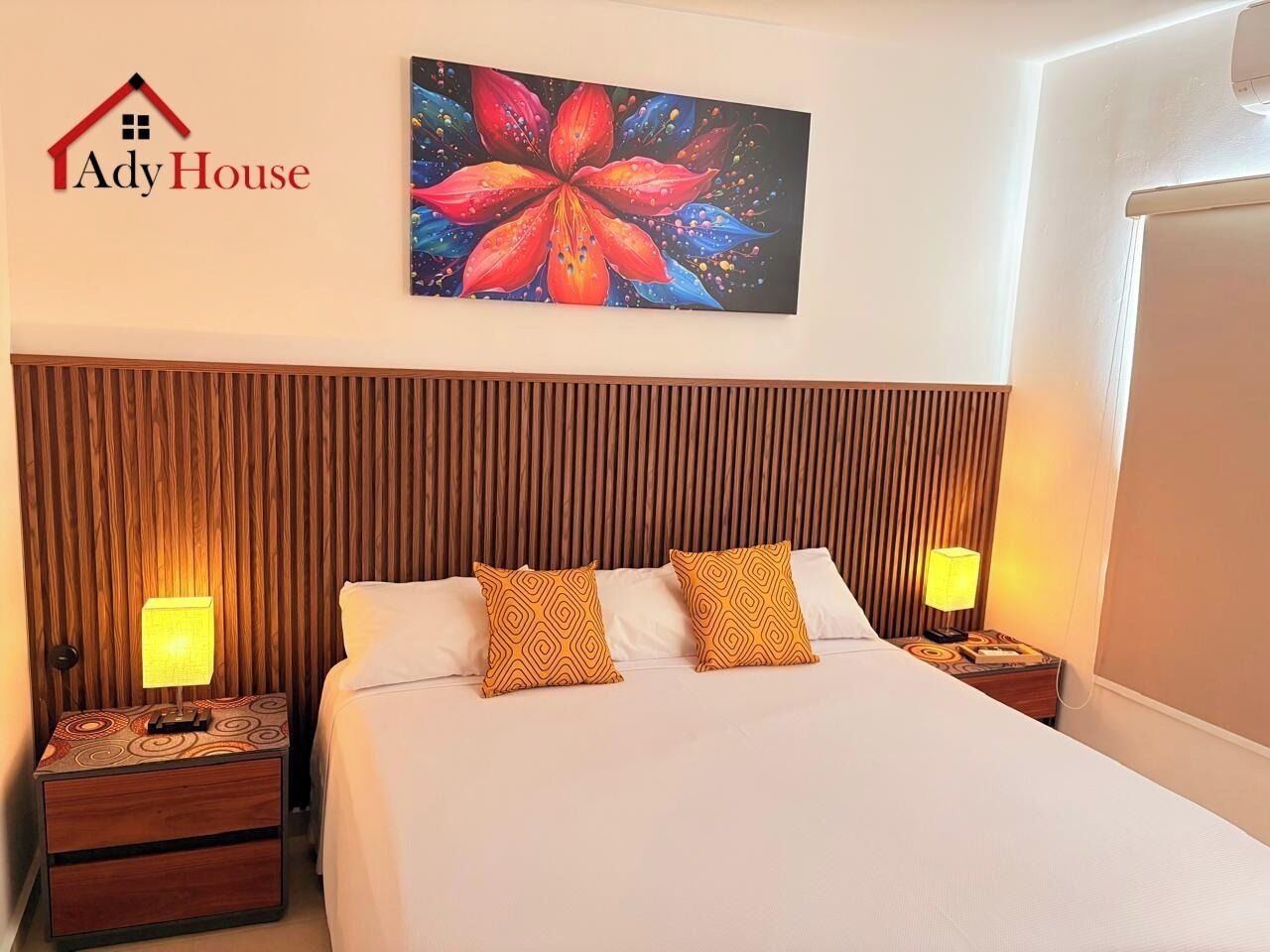 A hotel room with a large bed, two nightstands, a wooden headboard, and a floral painting on the wall.