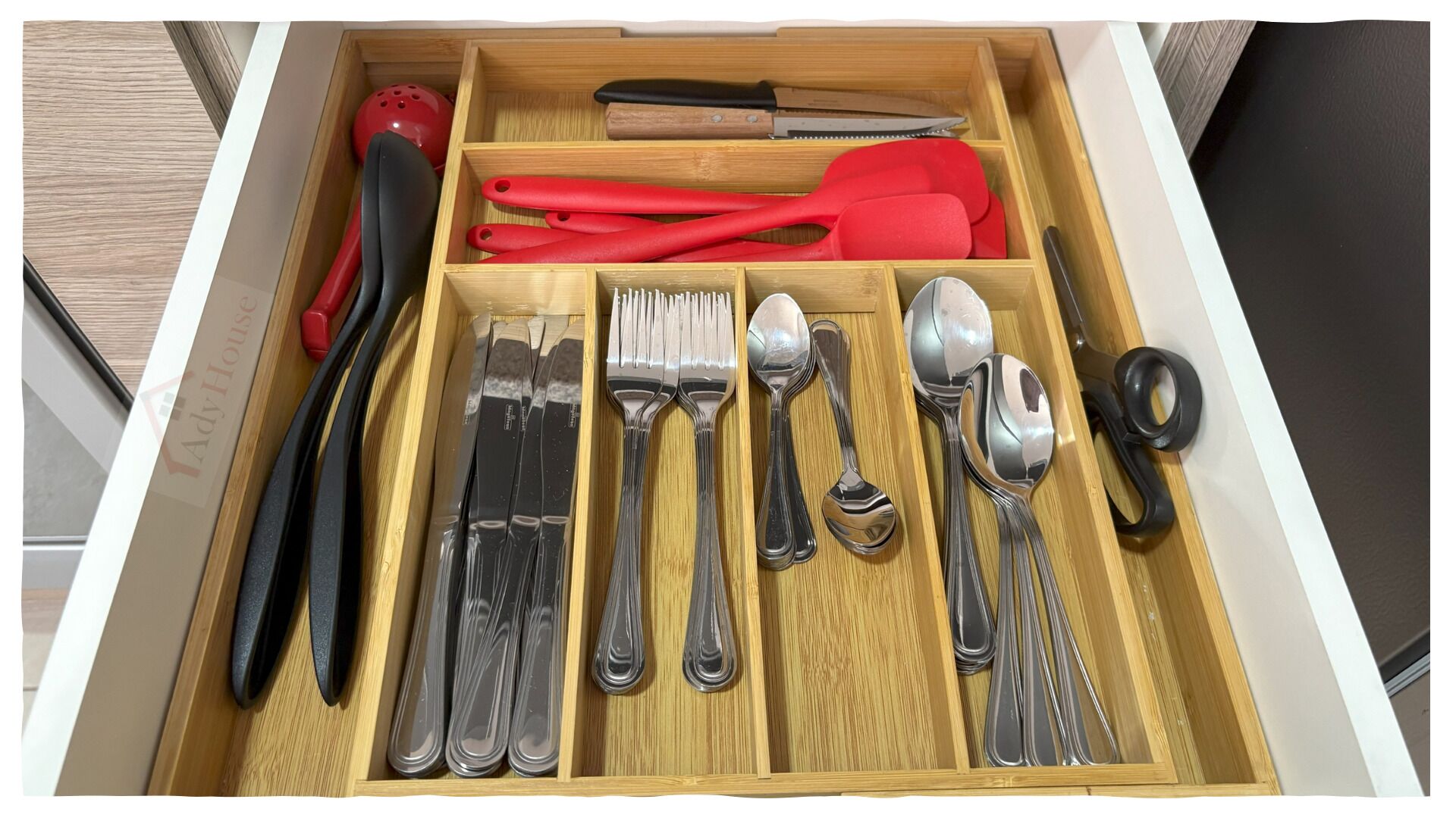 A drawer with neatly organized kitchen utensils including forks, spoons, and a red spatula.