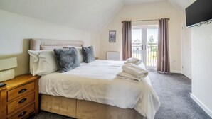 Une chambre à coucher avec un lit, une table de chevet en bois, un radiateur, une fenêtre avec des rideaux et une vue sur l’extérieur.