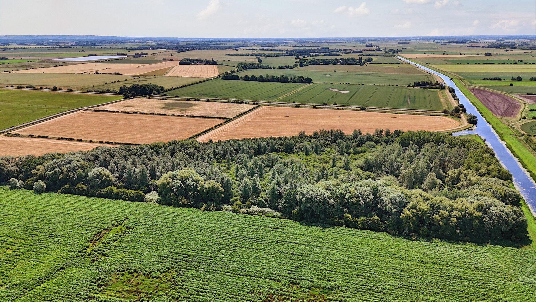 Une vue aérienne d’un paysage rural, avec des champs, une rivière et une forêt dense.
