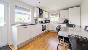 Une cuisine moderne avec des meubles blancs, un four encastré, un four à micro-ondes et un coin repas comprenant une table et des chaises.