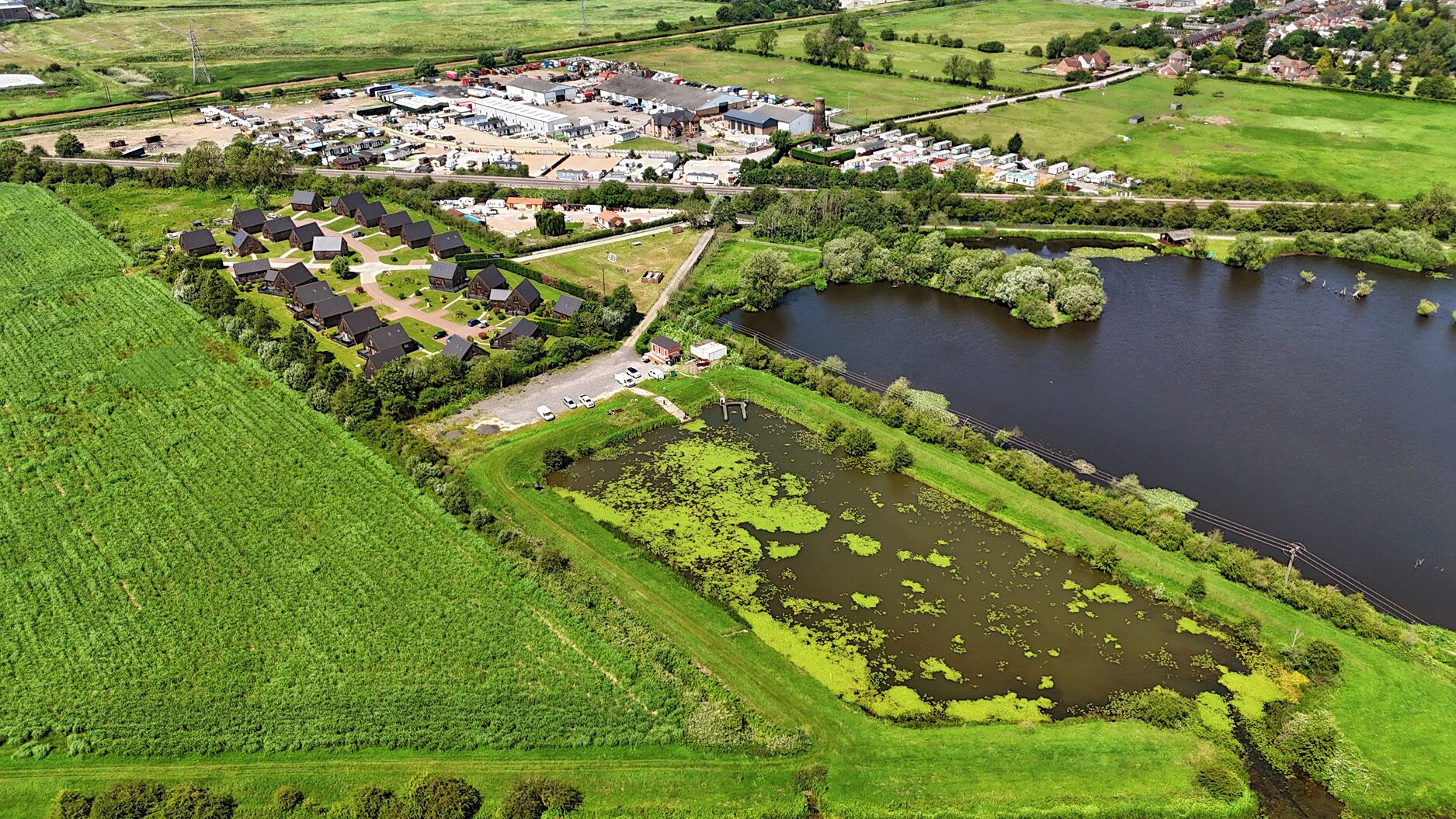 Une vue aérienne d’une zone rurale avec une étendue d’eau importante, une petite île et un ensemble de bâtiments auxquels mène une route.