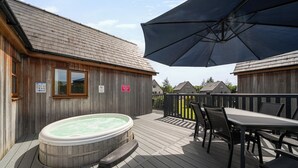 En træterrasse med et boblebad, et bord med stole og en stor parasol.