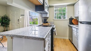 A kitchen with granite countertops, stainless steel appliances, and a window with a view of greenery.
