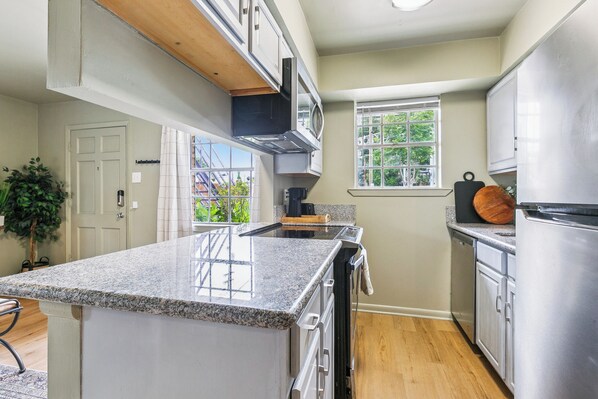A kitchen with granite countertops, stainless steel appliances, and a window with a view of greenery.