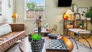 A living room with a brown leather sofa, a wooden coffee table with a chessboard, a lamp, and a TV mounted on the wall.