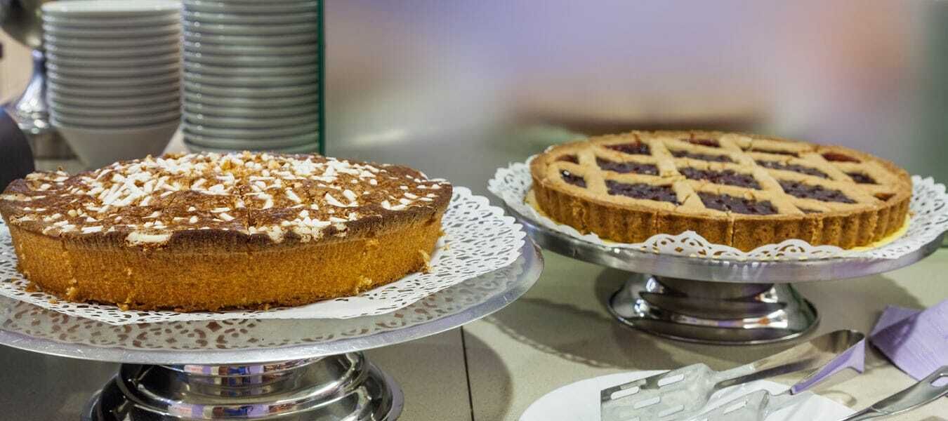 Two cakes on silver cake stands with lace doilies, a stack of plates, and a napkin holder.