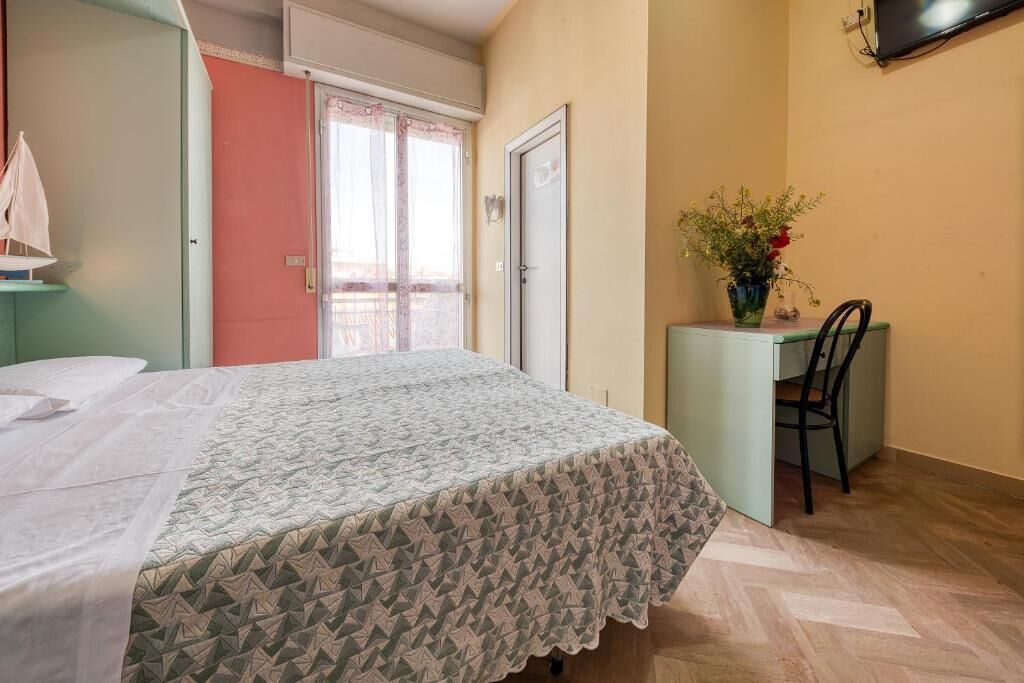 Um quarto com uma cama, uma escrivaninha com cadeira, uma janela com cortinas e uma porta.