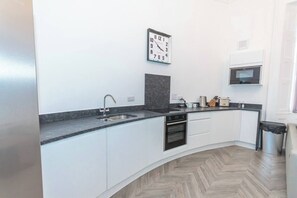 Cozinha moderna com armários brancos, bancada de granito, forno embutido e micro-ondas.