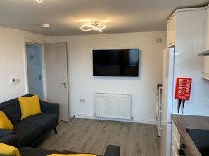 A modern living room with a sofa, a flat-screen TV, a white radiator, and a fire blanket mounted on the wall.