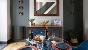 Een eetruimte met een glazen tafel, blauwe stoelen, een houten kast met spiegel en een bord op de muur.