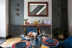 A dining area with a glass table, blue chairs, a wooden cabinet with a mirror, and a sign on the wall. - 2 bed house near Devonport Dockyard Plymouth (Plymouth)
